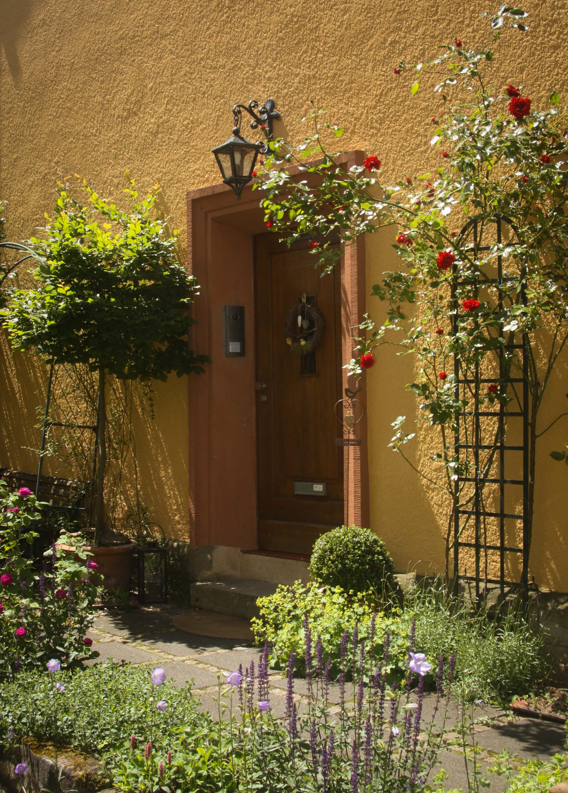Eingangstür zum Haus der Ferienwohnung umsäumt von viel Grün und blühenden Pflanzen, wie Lavendel oder Rosen.