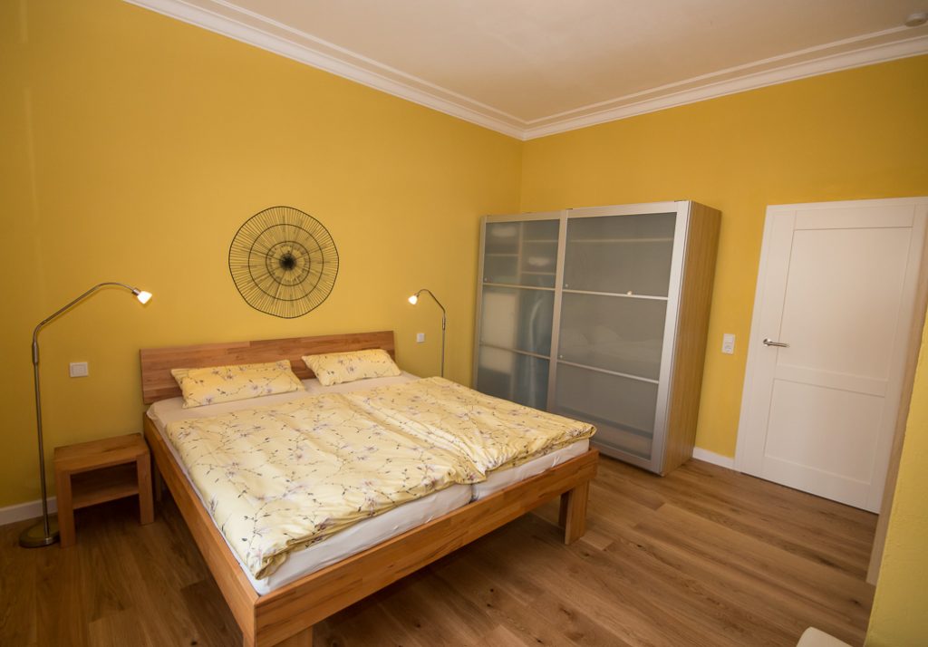 Angenehm leuchtend gelb gestrichenes Schlafzimmer der Ferienwohnung mit Doppelbett und großem Kleiderschrank.